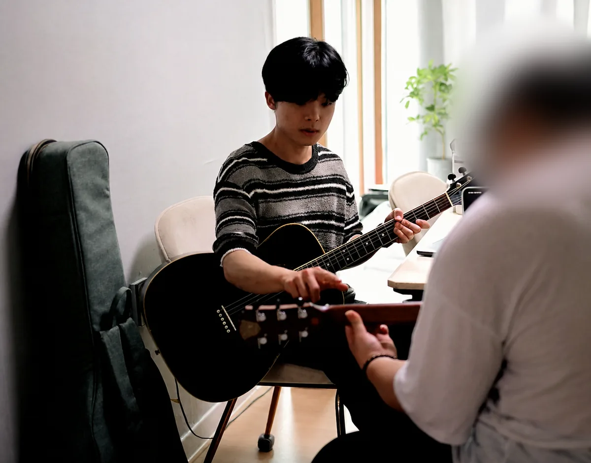 강사가 수강생의 기타 운지 위치를 손으로 가리키며 설명하는 실제 수업